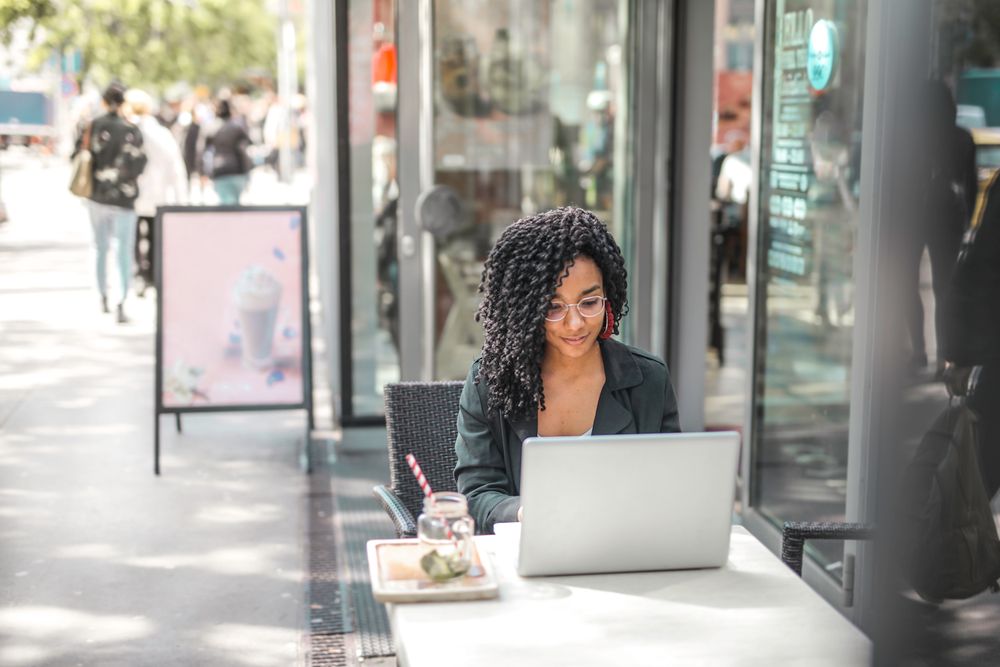 A woman working on a laptop at a sidewalk cafe table
