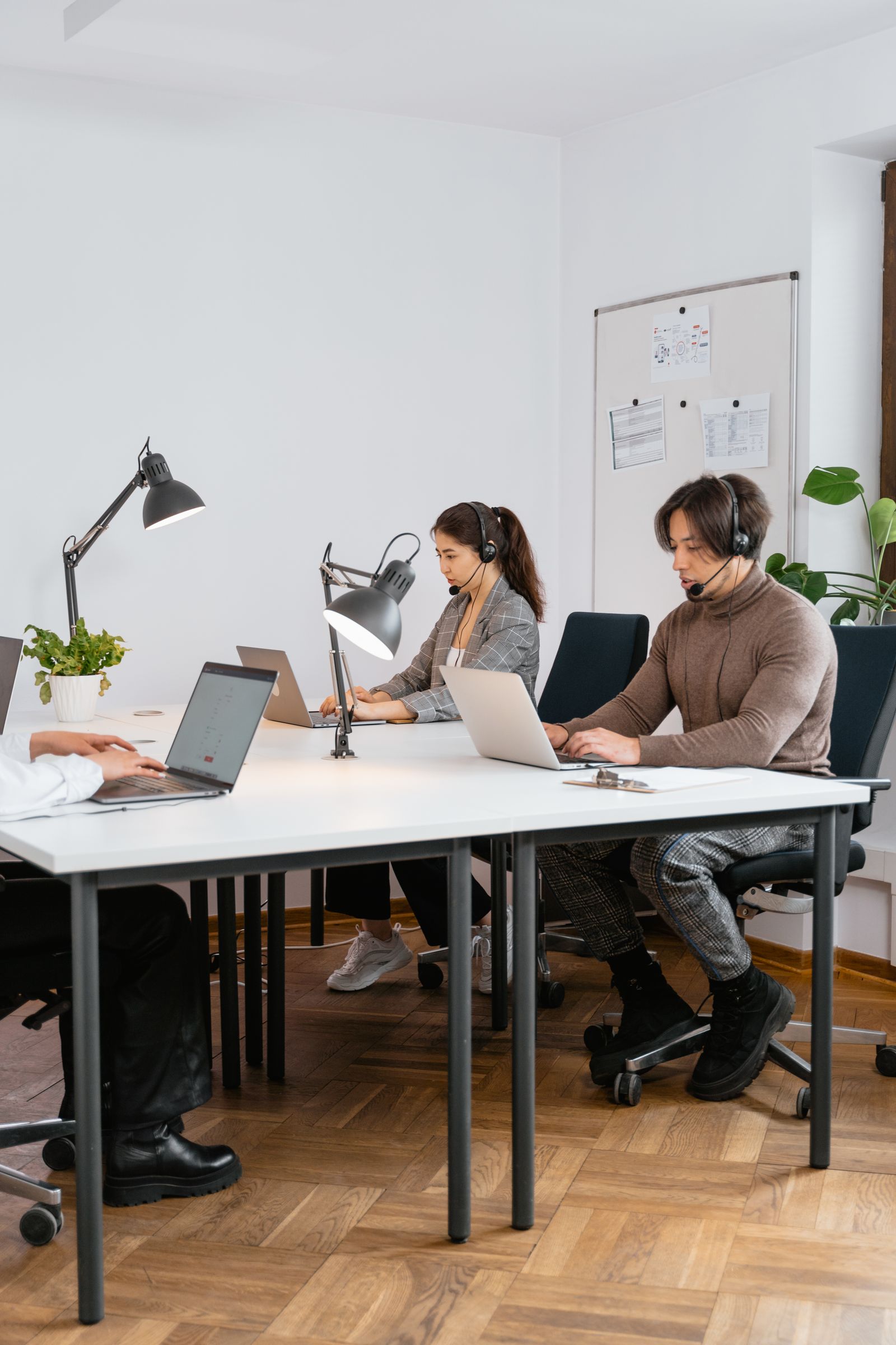 Two support team members wearing headsets take calls at a shared desk in a bright office