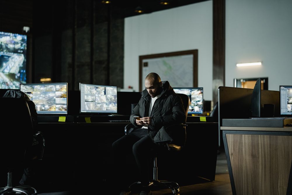 An operator at a monitoring desk in front of a wall of live status screens