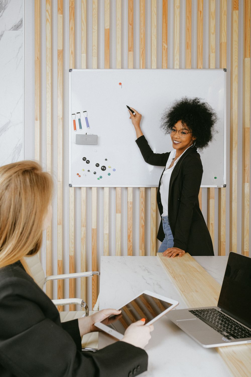 A woman presenting at a whiteboard to a colleague holding a tablet